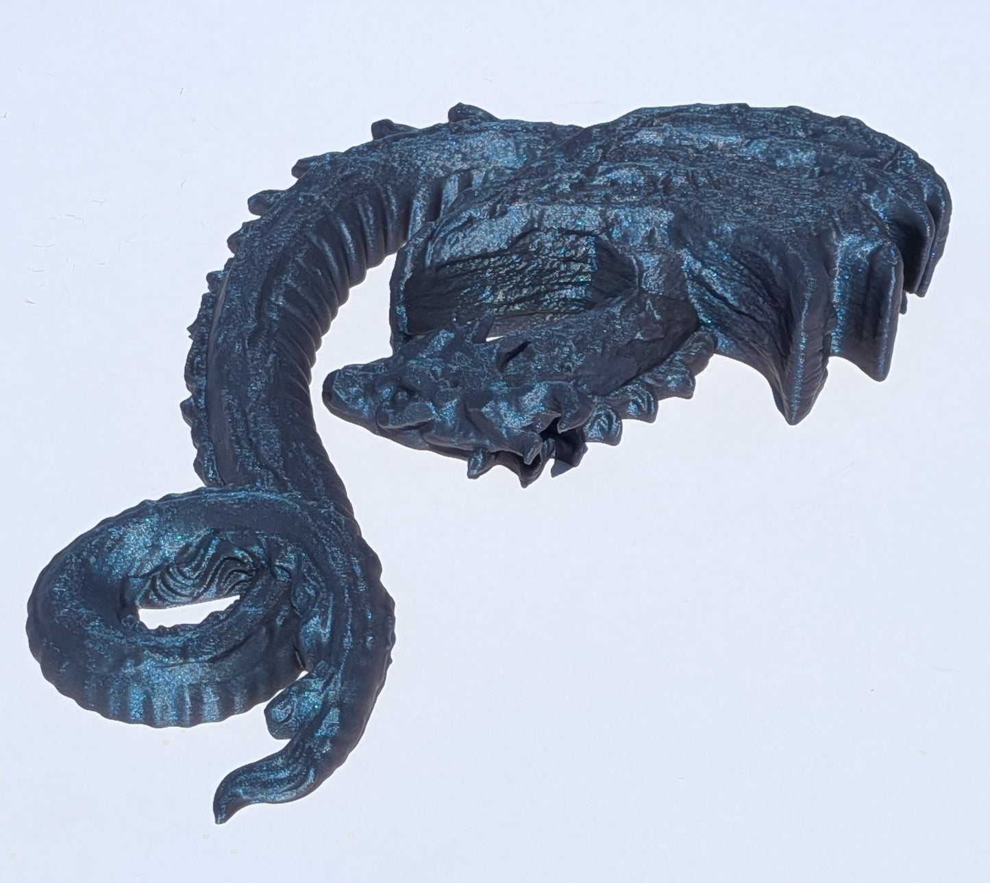 A dark metallic blue dragon skull sculpture or decorative piece, shown against a plain light gray background.