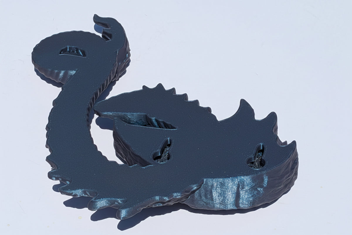 A dark metallic dragon figurine or wall decor piece shown from the back, featuring a textured, reflective finish, set against a plain light background.