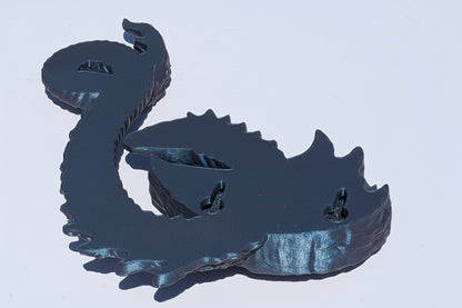 A dark metallic dragon figurine or wall decor piece shown from the back, featuring a textured, reflective finish, set against a plain light background.