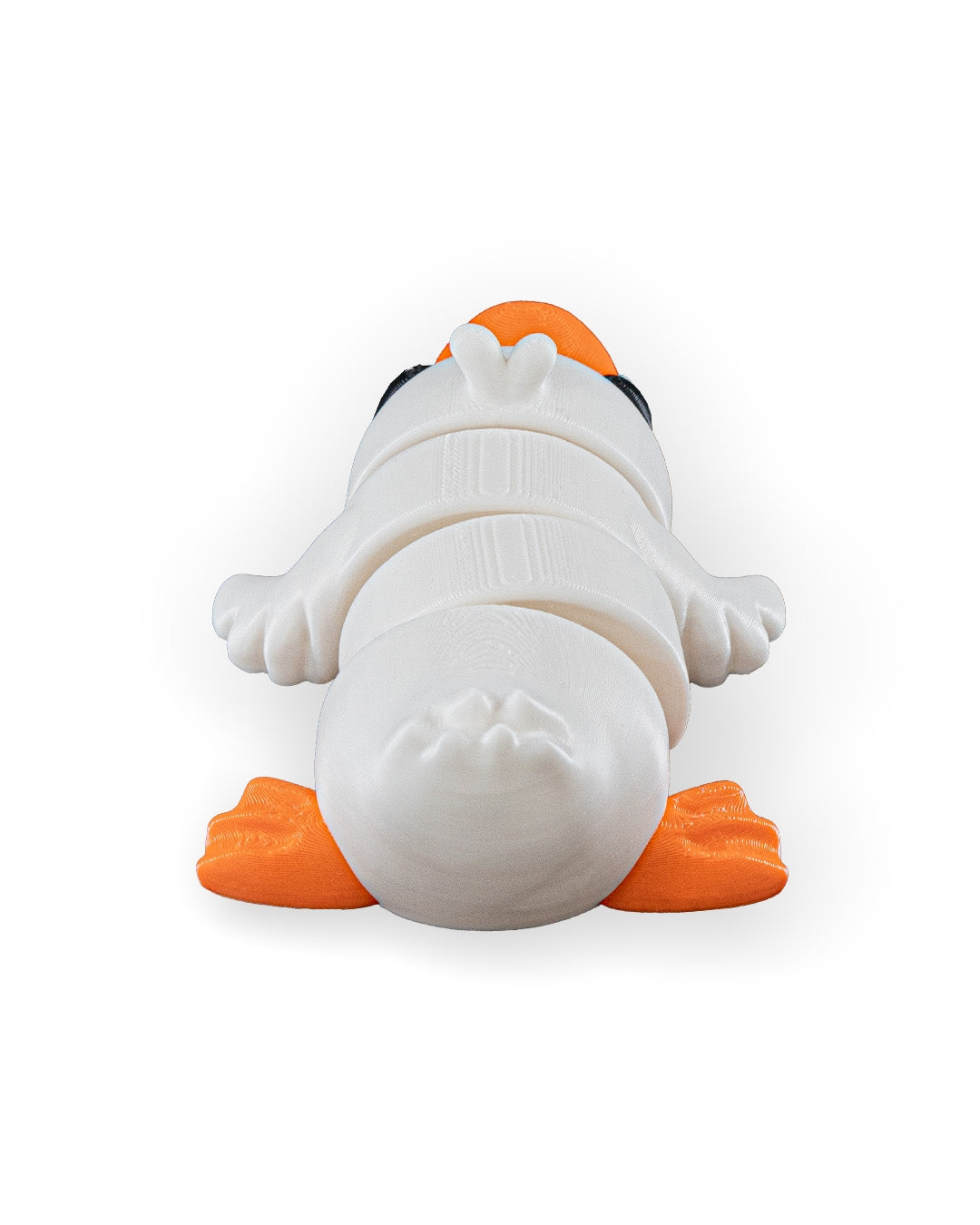 A white plastic toy penguin lying on its back, featuring bright orange feet and beak, set against a plain white background.