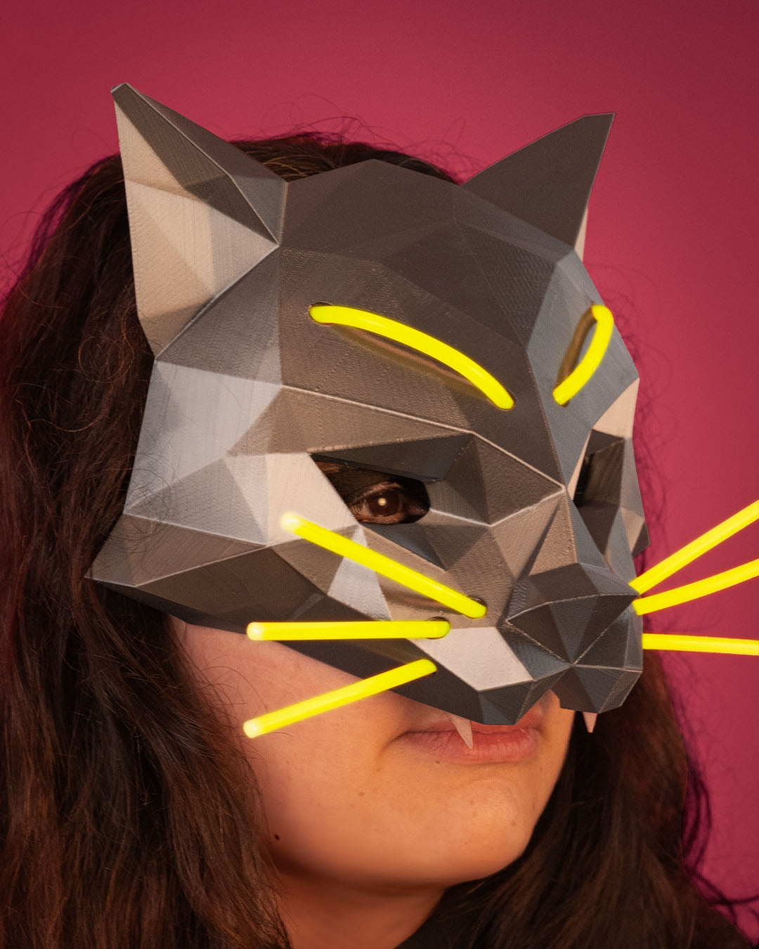 Person wearing a geometric cat mask with yellow accents against a pink background
