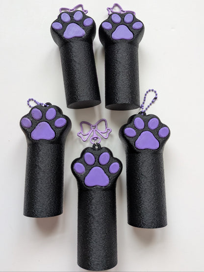 Five black cylindrical chapstick bagcharms with purple paw print screw on lid hanging from purple ball chain or purple bow lobster claw keychain, arranged on a plain white background.