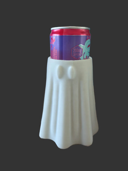 A white ghost-shaped can cooler holding a purple and red beverage can, set on a wood-patterned surface with a blue display board in the background.