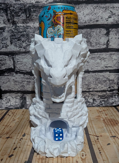 A white dragon head can holder made of stone-like material, shown holding an L-Carnival beverage can on top and a blue die in the base, set against a gray brick wall and wooden surface.