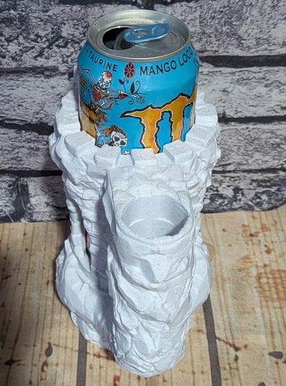A white, crumpled-paper style can holder shaped like a rock or textured sculpture, shown holding a blue Monster Energy drink can on a wooden surface against a gray brick-patterned background.