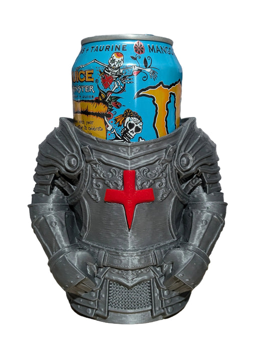 A gray knight armor mug holding a can of Monster Energy Drink, set on a wooden surface against a gray brick wall background.
