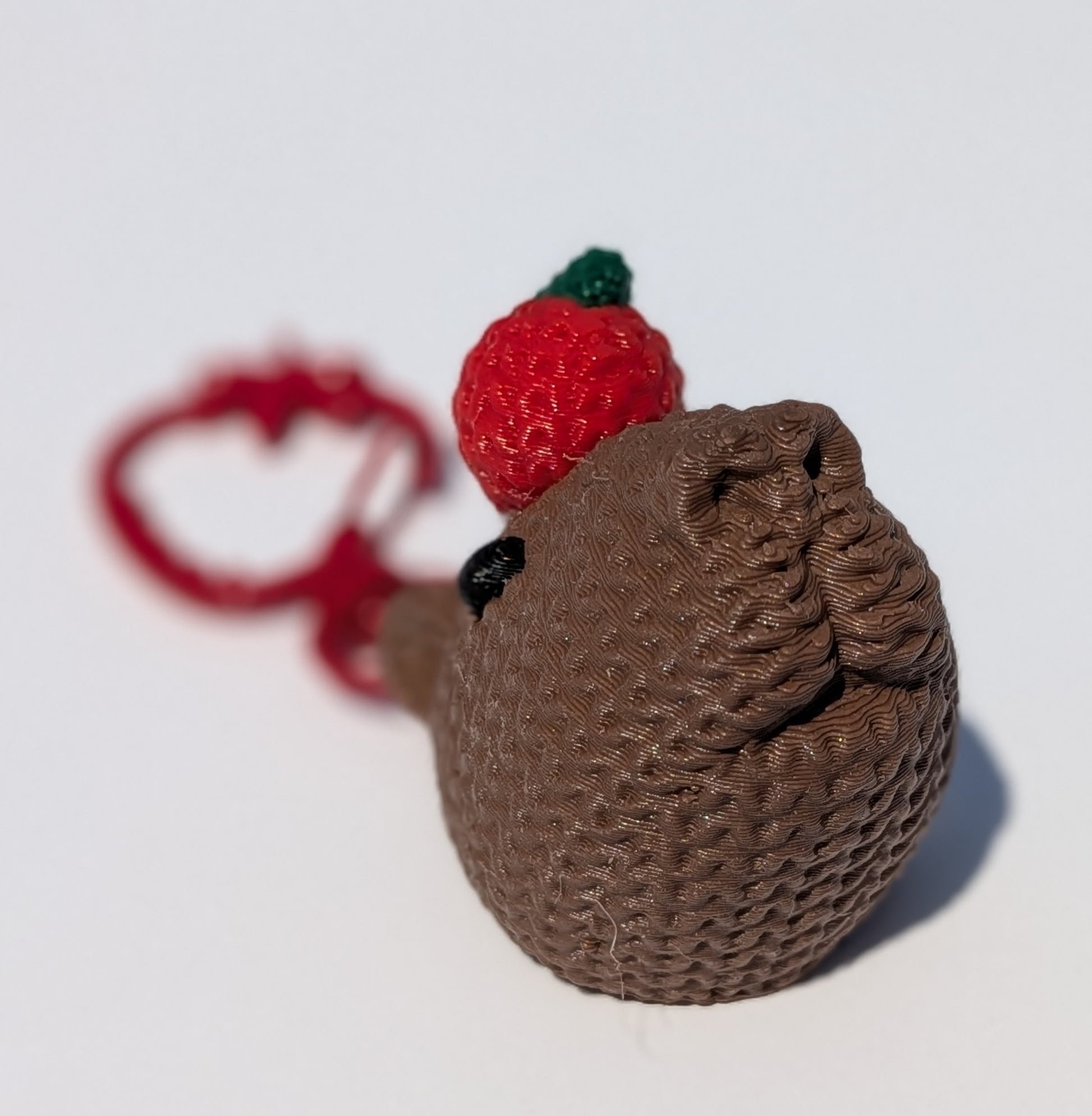 A small brown textured plush toy or pouch with a red strawberry accent and a red loop at the top, photographed on a plain white background.