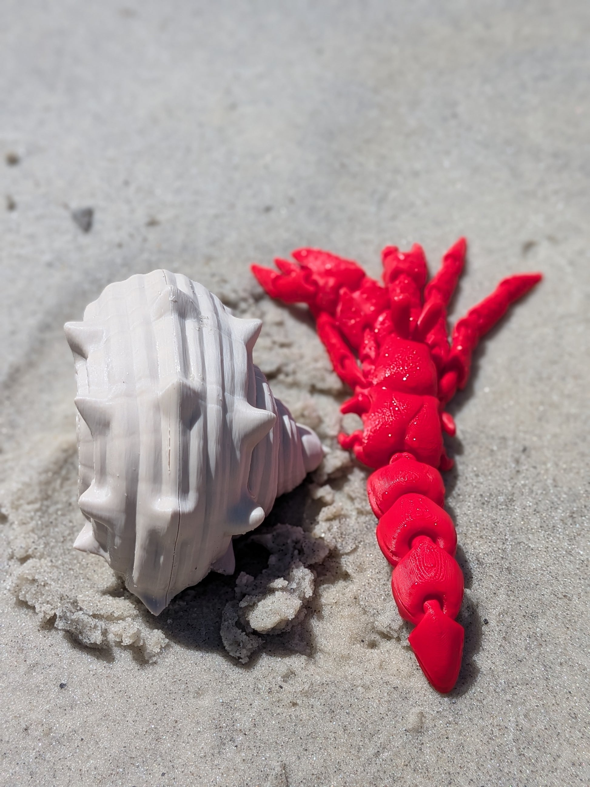 A white seashell and a bright red braided cord or hair accessory placed on light gray sand.