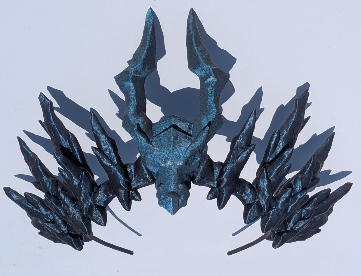 A metallic blue and black fantasy horned headpiece or mask with sharp angular horns and leaf-like wing-like extensions on both sides, photographed against a plain light background.