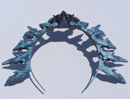 A metallic silver headband styled with icy blue and silver leaf-like spikes, photographed against a plain white background with a distinct shadow.