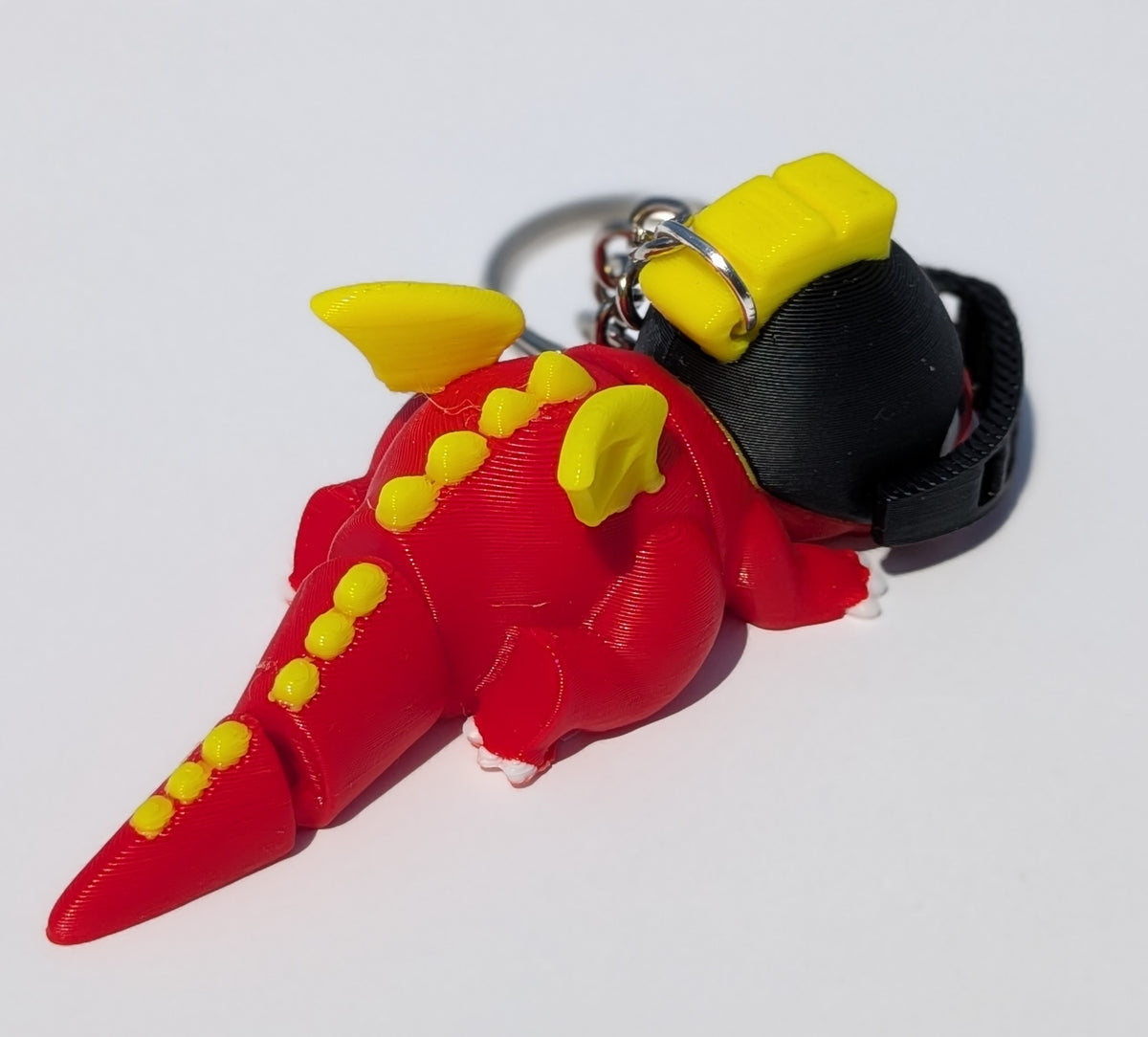 A 3D-printed dinosaur keychain in red and yellow, featuring a black strap and metal keyring, photographed on a plain white background.