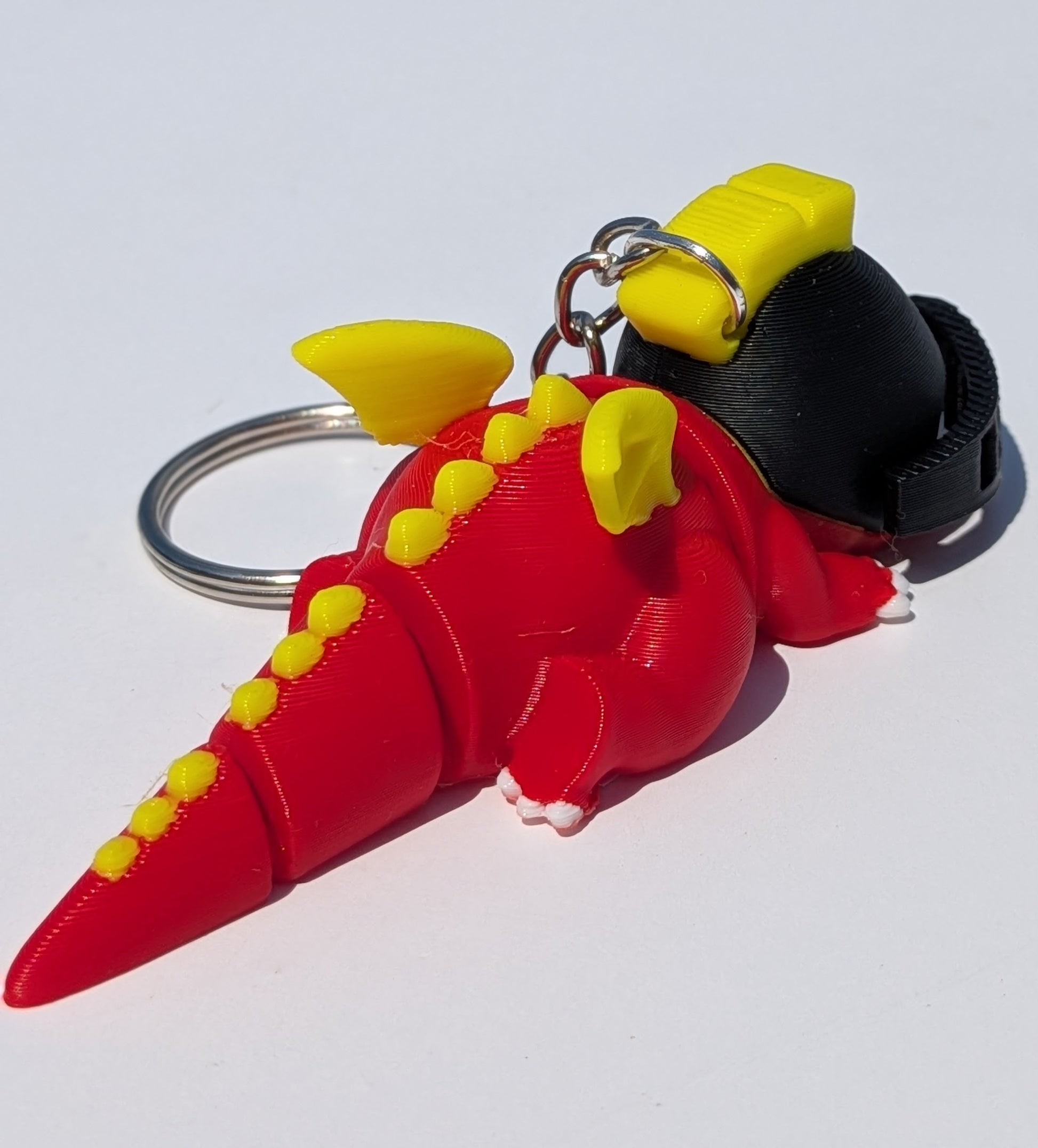 A 3D-printed red dinosaur keychain with yellow spikes and yellow wing-like details, attached to a black strap and metal key ring on a plain white background.