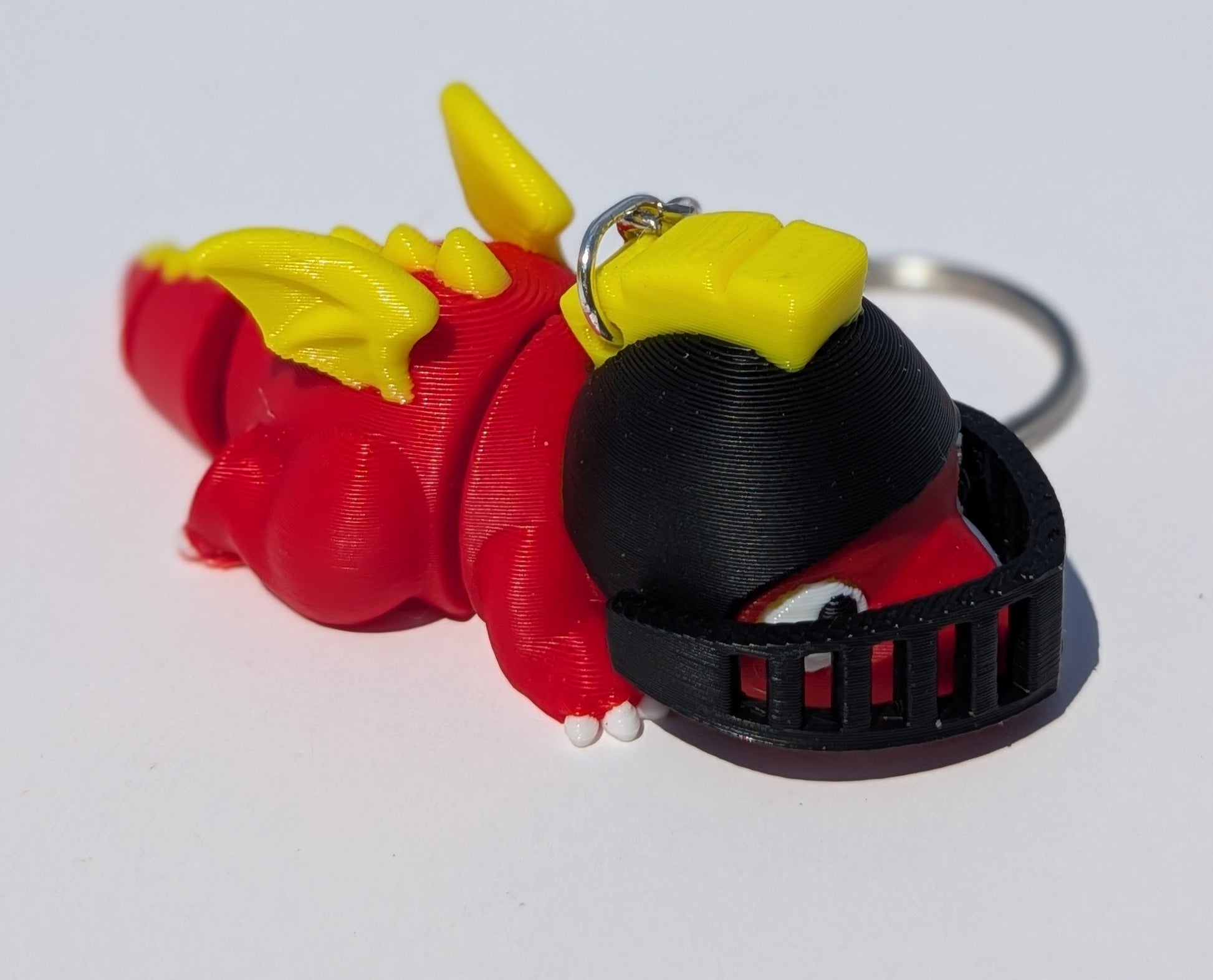 A 3D-printed dragon keychain in red and yellow, wearing a black helmet, shown on a plain white background.