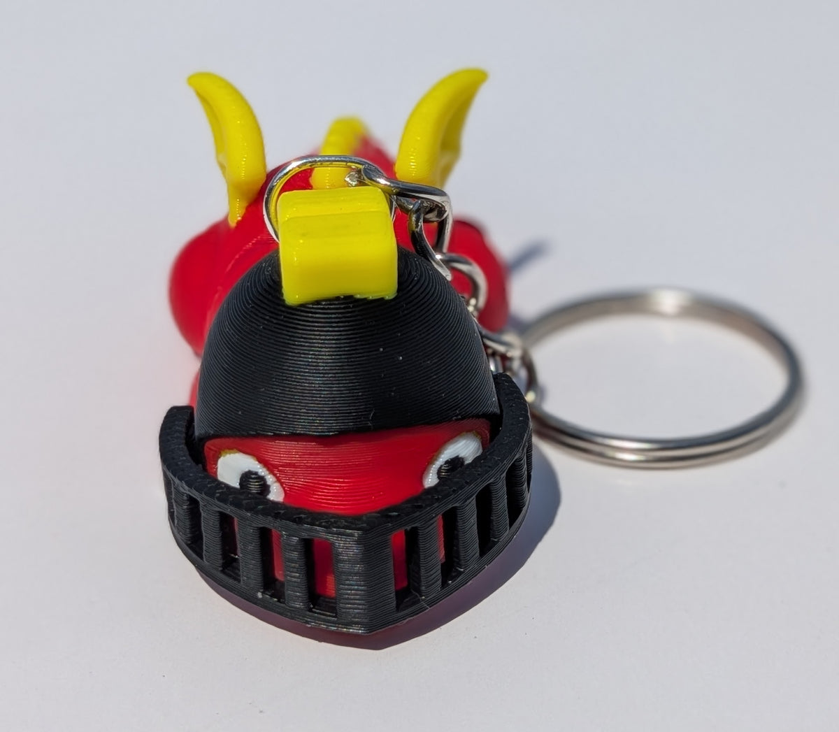 A 3D-printed keychain shaped like a red and black monster or creature with yellow horns, attached to a silver metal key ring on a plain white background.