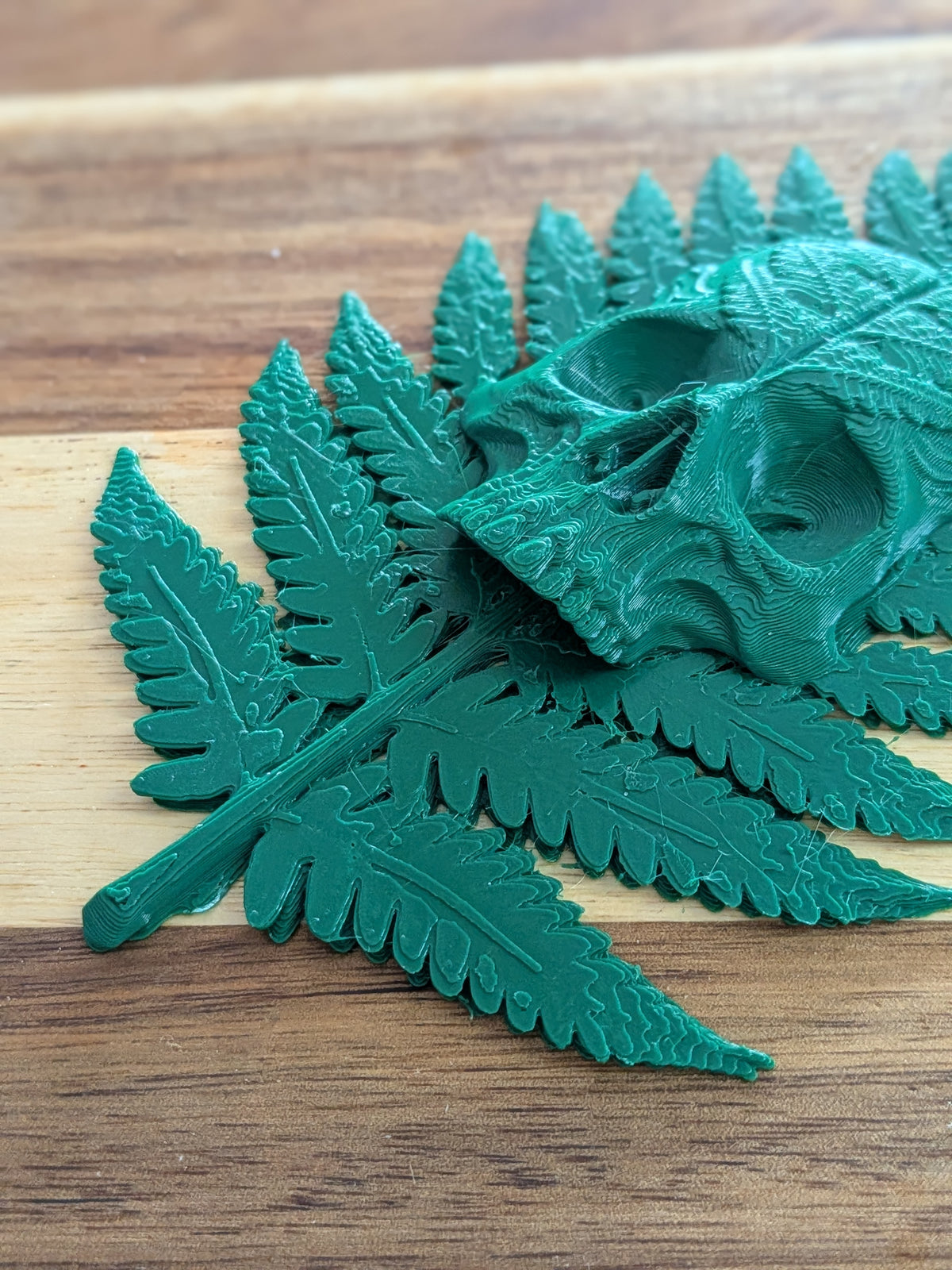 A 3D-printed green skull and fern leaves displayed on a wooden surface.