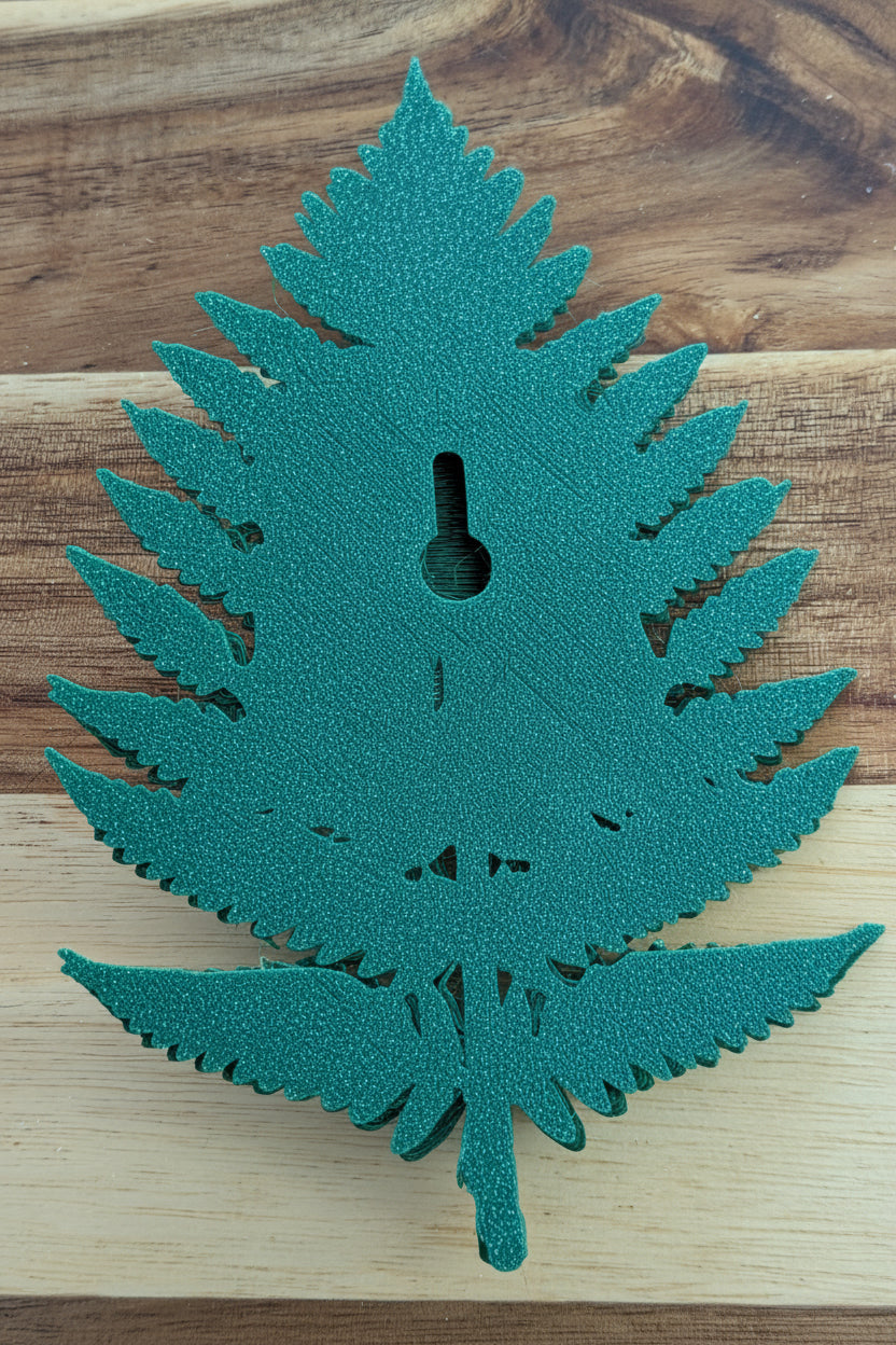 A green fern-shaped decorative object with a keyhole cutout in the center, placed on a wooden surface. A small white price tag reading $5 is attached near the middle.