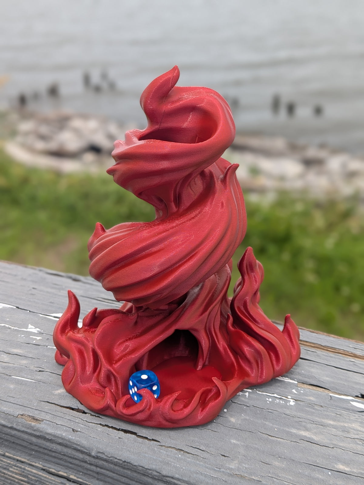 Flame dice tower outdoors on a wooden railing with a blue die in the tray