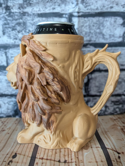 A lion-shaped ceramic mug with a detailed mane and tree trunk handle, shown holding a black can on a wooden surface against a gray brick wall background.