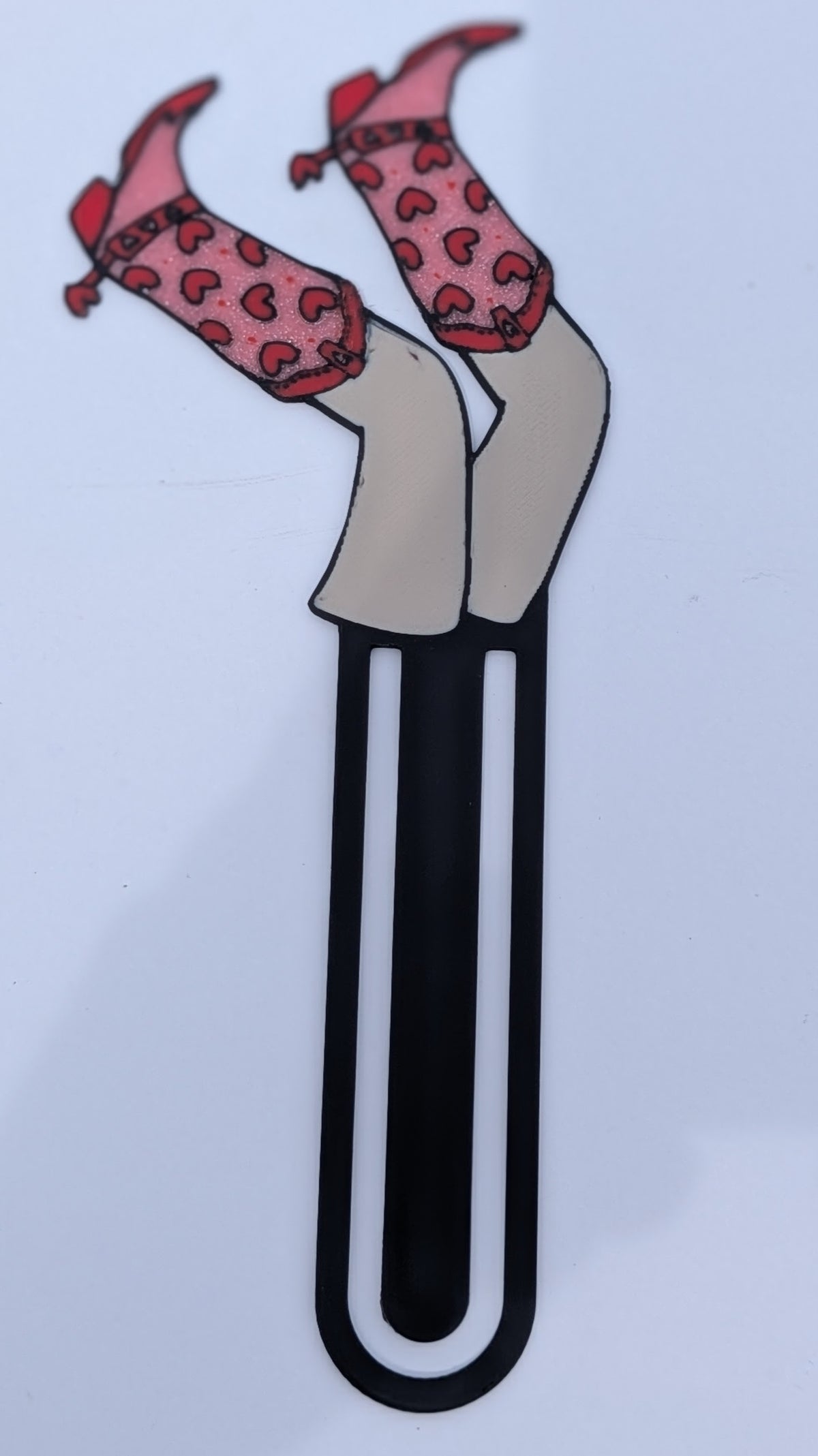 Bookmark shaped like legs in pink heart-print cowgirl boots, clipped over a book page