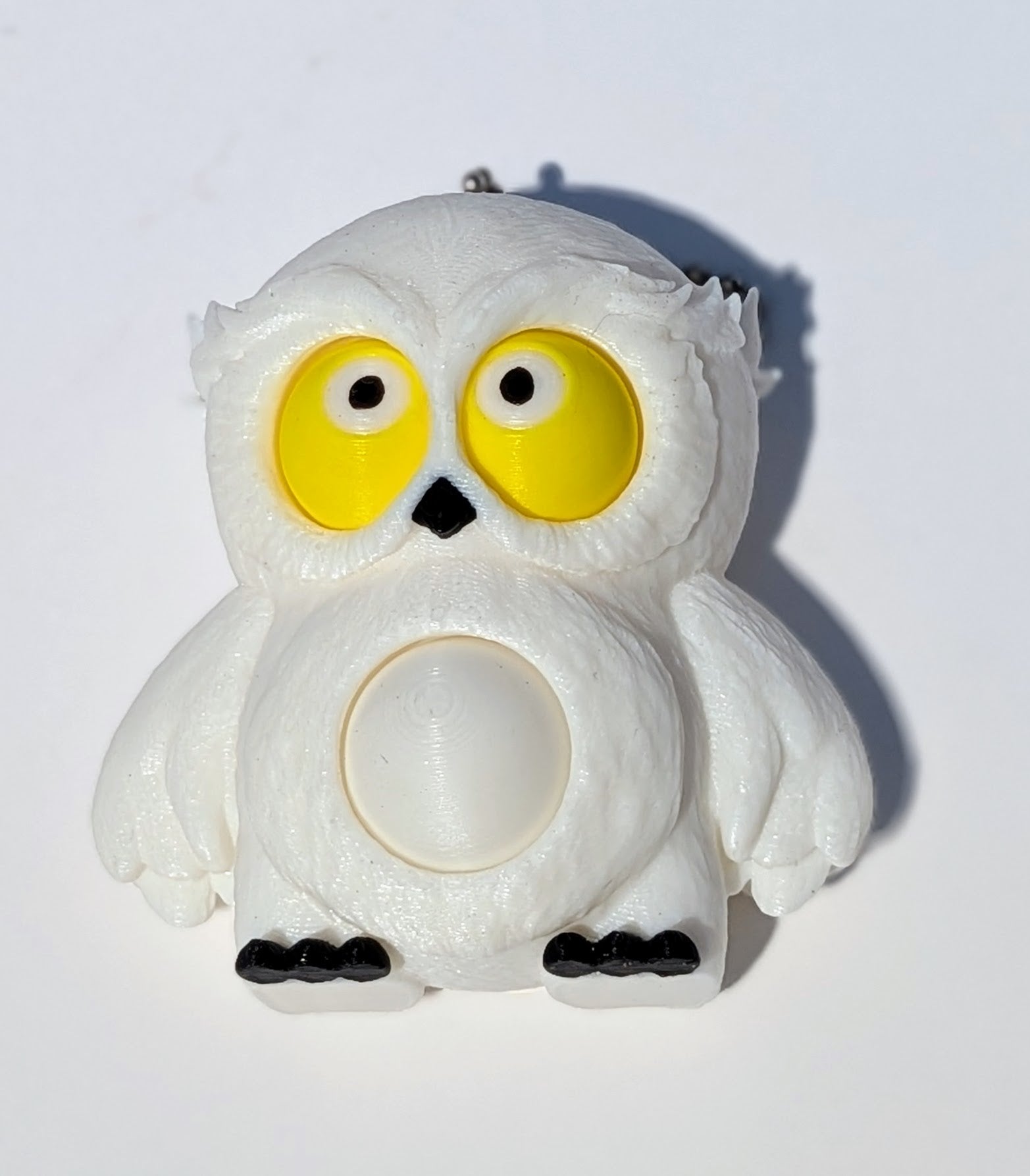 A white owl-shaped novelty item with large yellow eyes, black feet and beak, photographed on a plain white background.