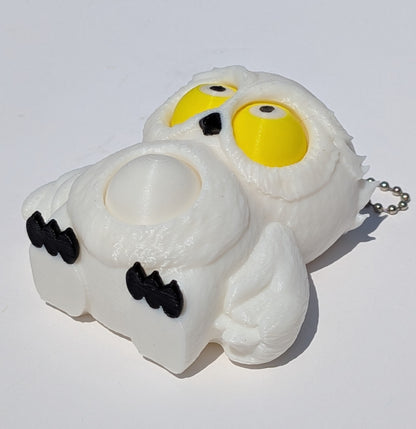 A white, textured, squishy ghost-shaped keychain or pouch with large yellow eyes, black whiskers, and a silver ball chain, photographed on a plain white background.