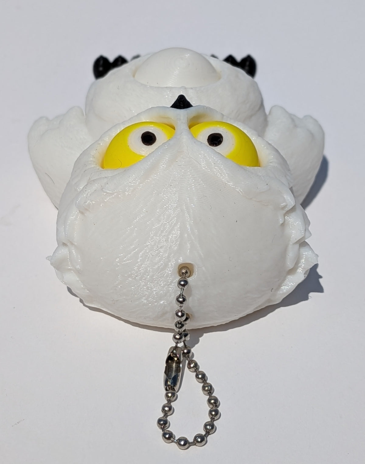 A white plush owl toy with large yellow eyes, black ear patches, and a silver ball chain keychain, photographed on a plain white background.