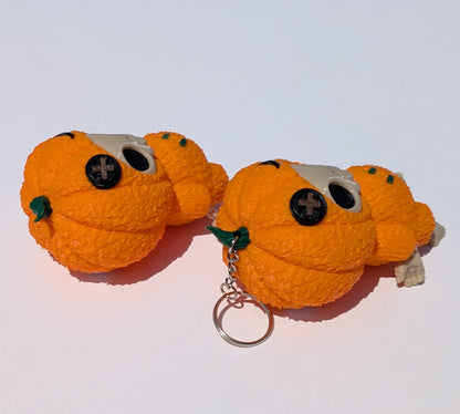 Two small orange pumpkin-shaped keychain toys with black button eyes, green leaf accents, and silver metal key rings on a plain white background.