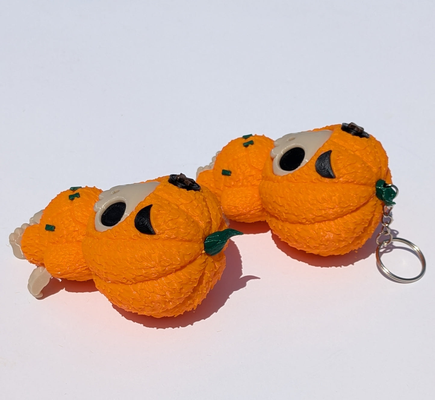 Three small orange pumpkin-shaped keychains with black eyes and green stems, arranged on a plain white background.
