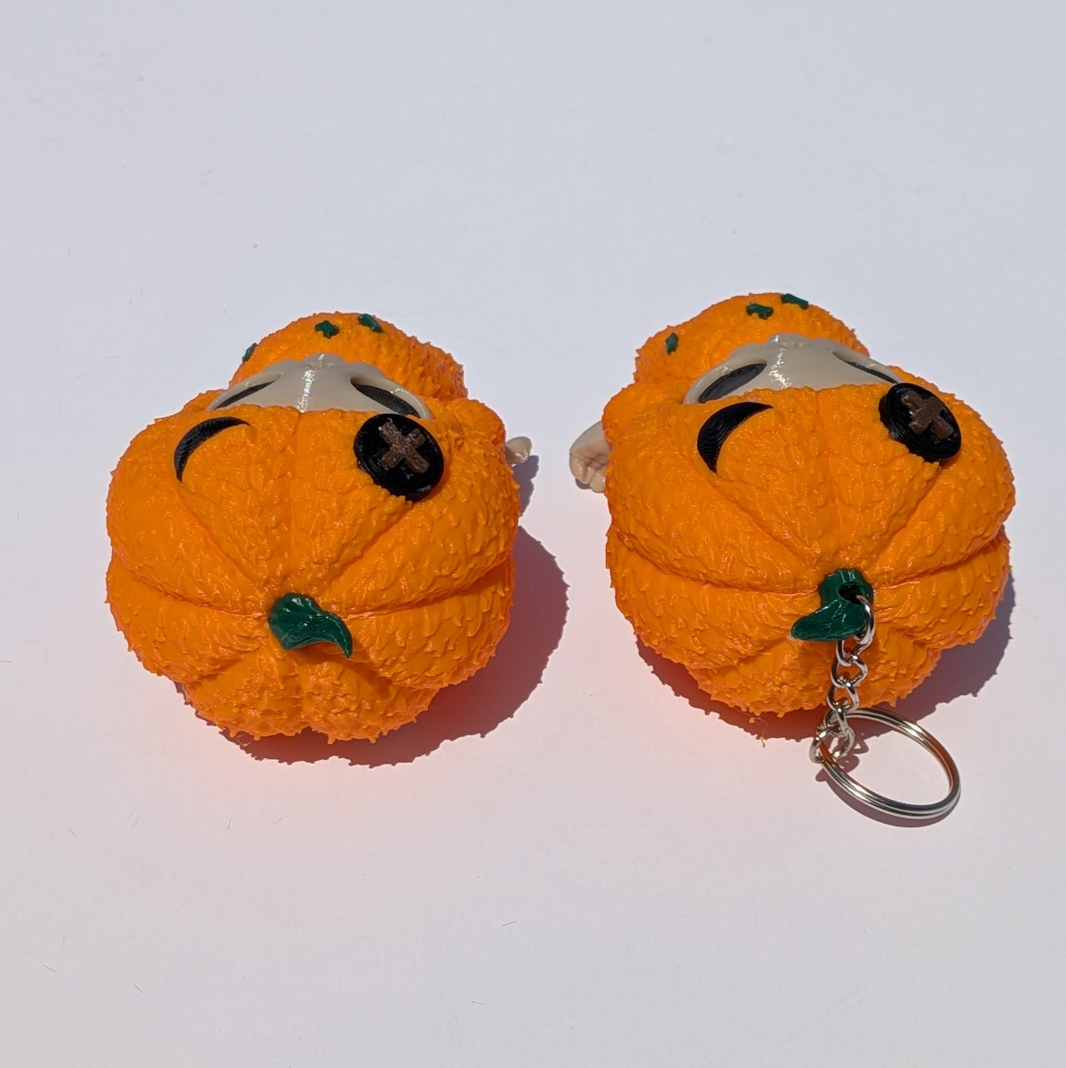 Two small orange pumpkin-shaped keychains with black eyes and green stems, photographed on a plain white background.