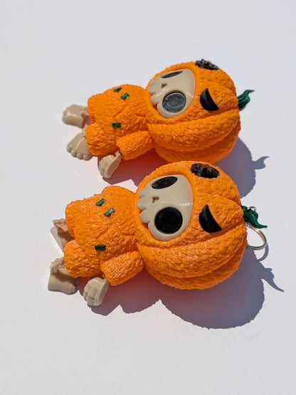 Two small orange pumpkin-shaped plush toys with cream-colored faces, black eyes, and green stems, photographed on a white background with strong sunlight and shadows.