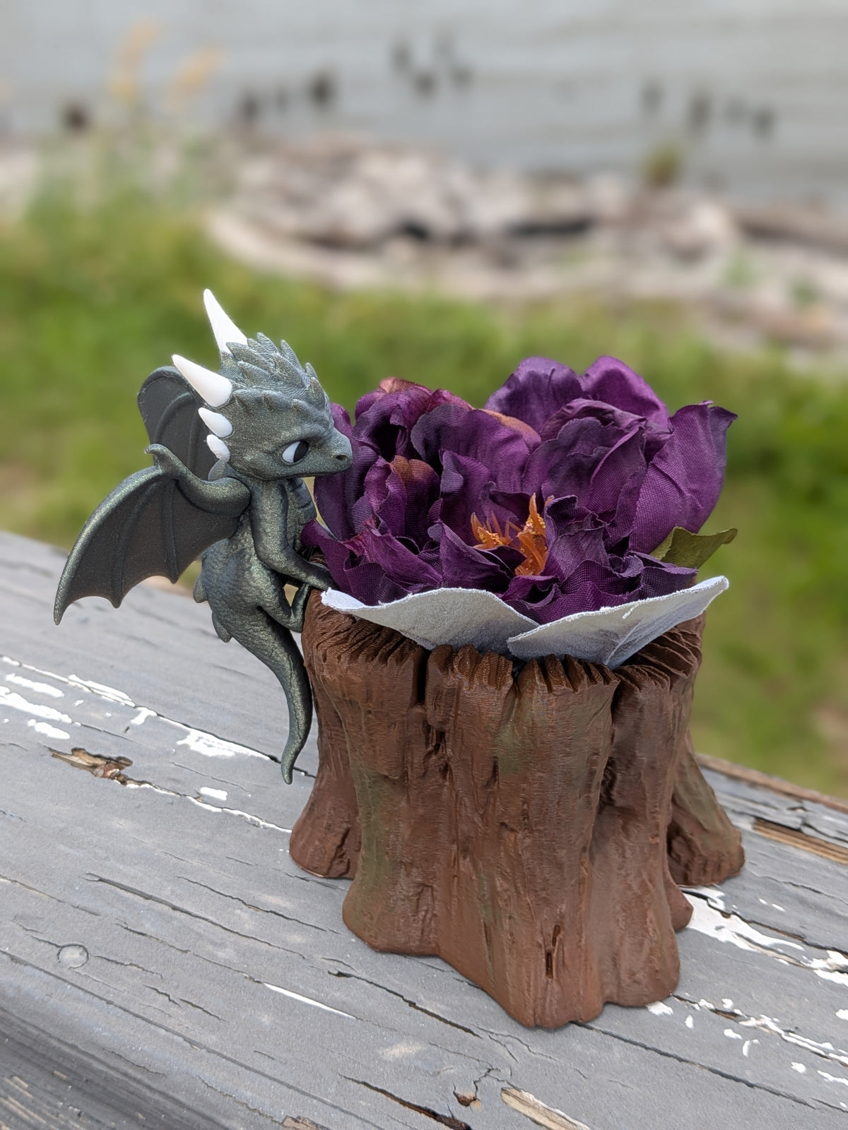 Baby dragon perched on a tree stump planter filled with purple flowers