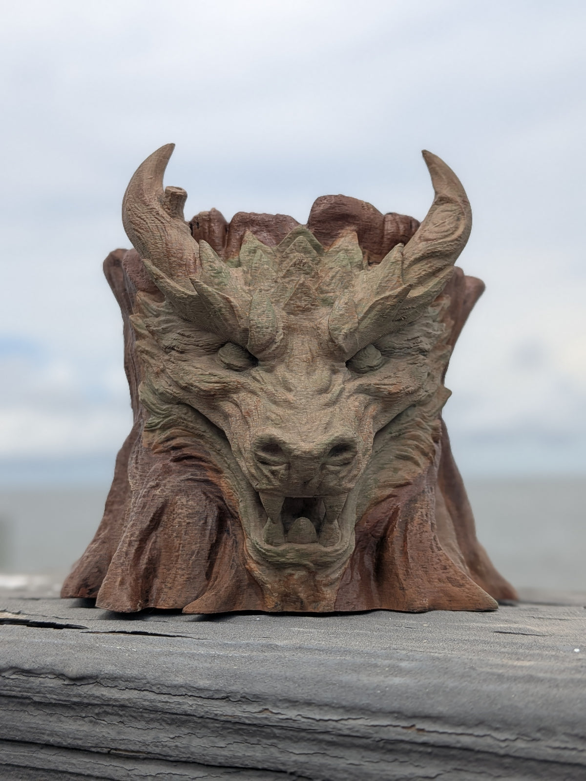Carved dragon face emerging from a tree stump planter, front view
