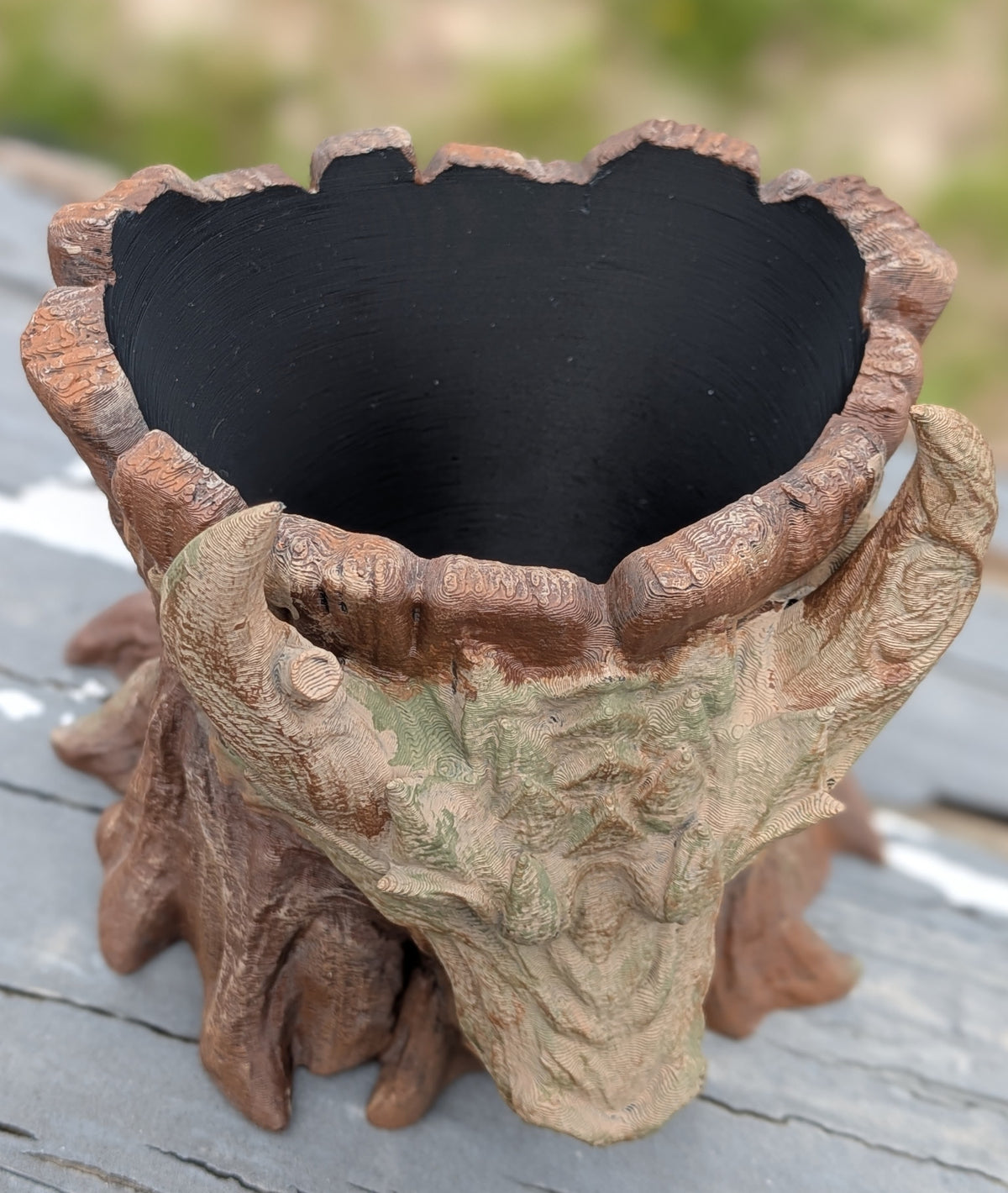 Dragon face stump planter displayed outdoors on a wood railing