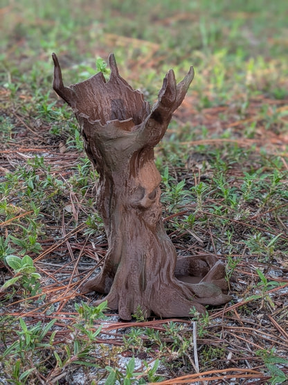 A small brown decorative tree stump sculpture with antler-like branches, placed outdoors on grass and pine needles.