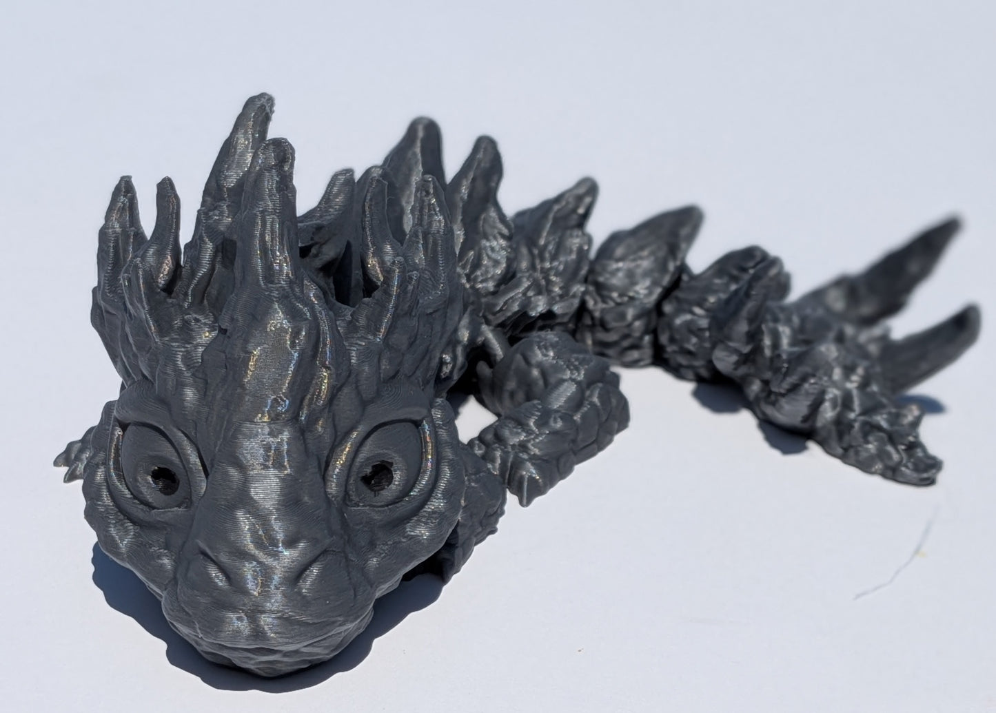 A dark gray 3D-printed articulated dragon figurine, shown from a low angle on a plain white background.