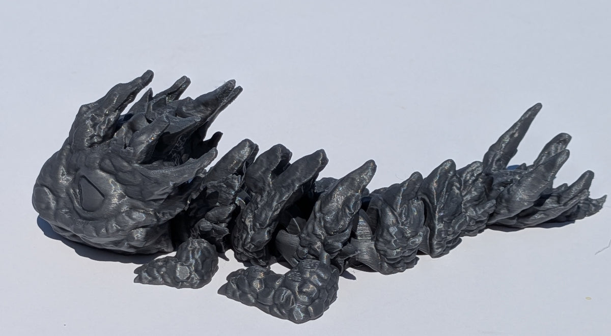 A dark gray, highly textured, and organic-shaped sculptural object with spiky, claw-like protrusions, photographed on a plain light gray background.