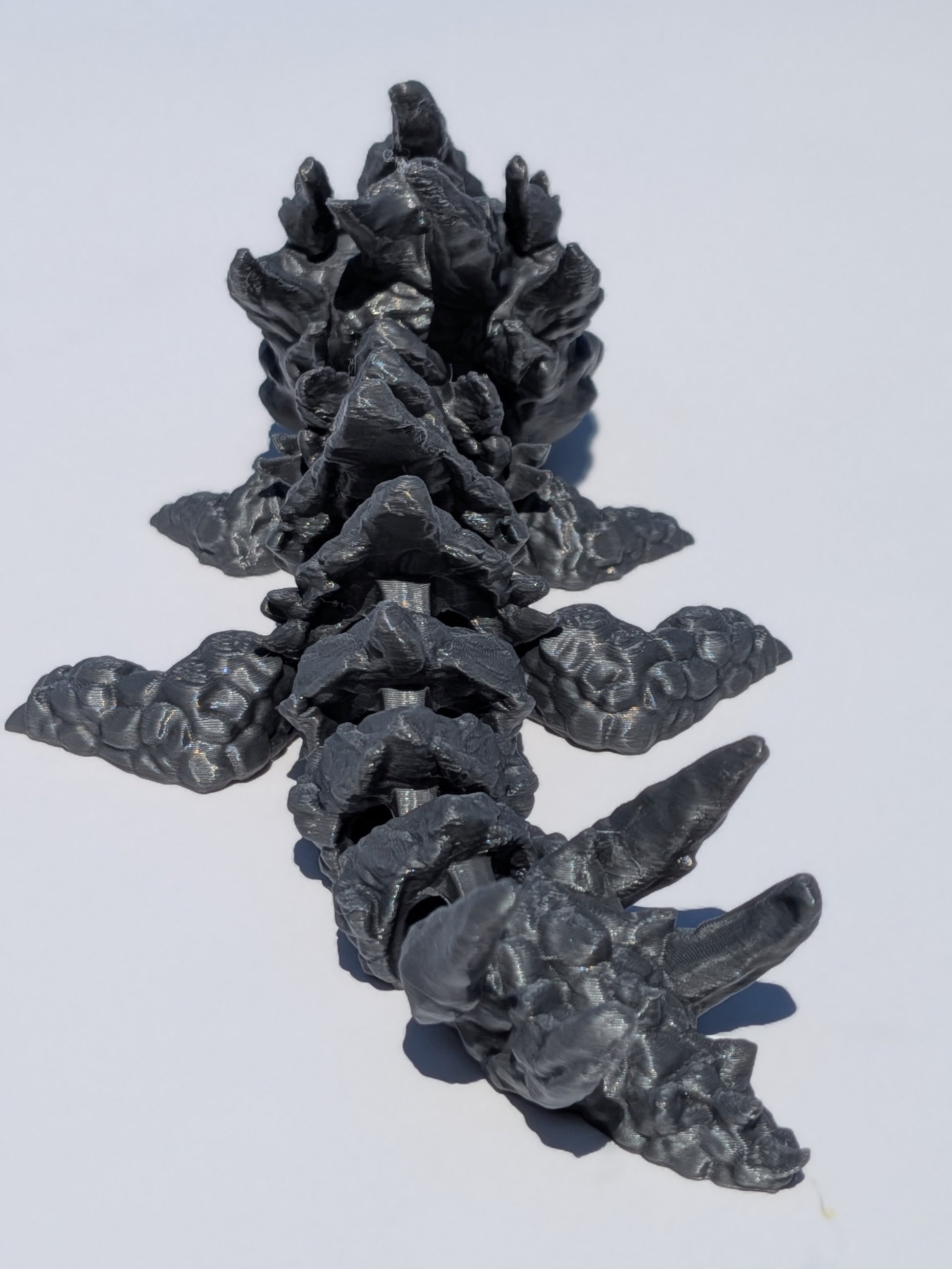 A dark gray 3D-printed articulated spine model, shown on a plain white background.